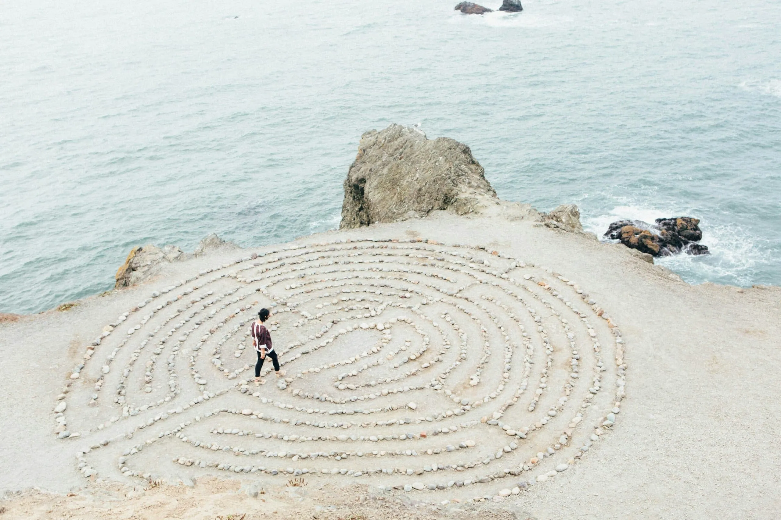 Person geht barfuß durch ein Steinlabyrinth am Meeresrand